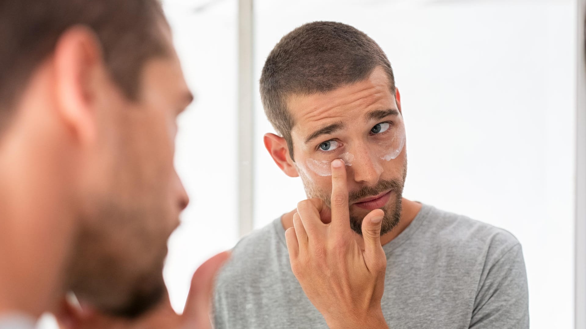 Ein Mann cremt sich die Haut unter den Augen ein. Ein Mann cremt sich die Haut unter den Augen ein.