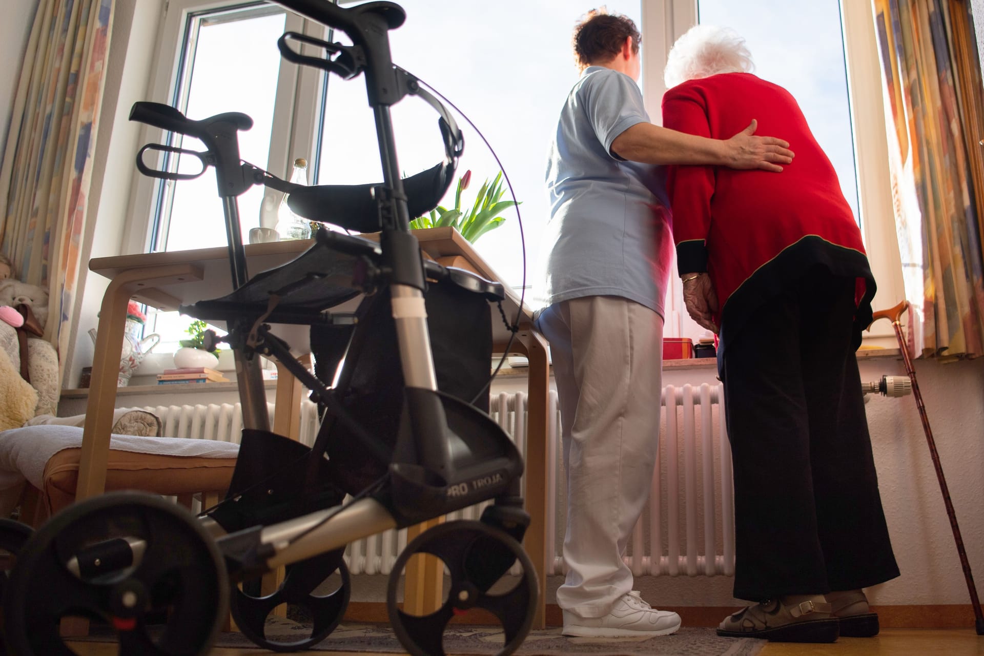 Eine Pflegerin steht mit einer Heimbewohnerin am Fenster: Das deutsche Pflegesystem steht vor zahlreichen Herausforderungen. Eine Pflegerin steht mit einer Heimbewohnerin am Fenster: Das deutsche Pflegesystem steht vor zahlreichen Herausforderungen.